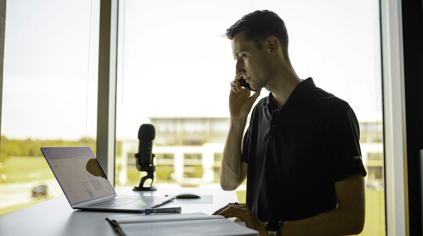 Man on a phone call at his desk with a laptop