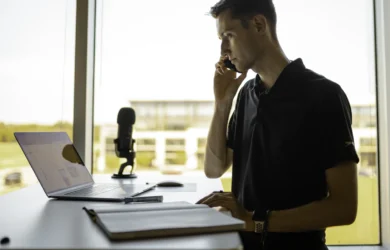 Man on a phone call at a standing desk with a laptop in a bright office