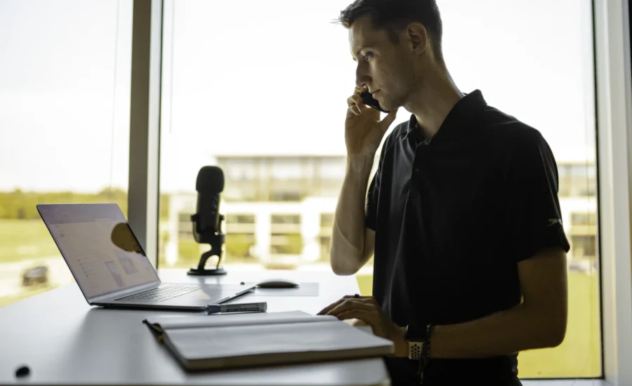Man on a phone call at a standing desk with a laptop in a bright office
