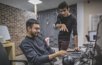 Two IT colleagues at a desk reviewing a laptop in a modern office