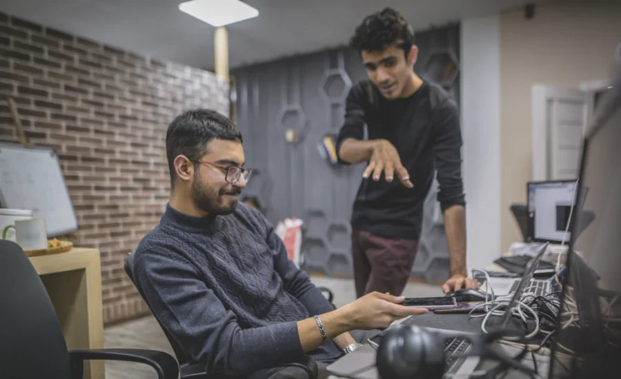 Two IT colleagues at a desk reviewing a laptop in a modern office