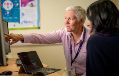 Two coworkers at an office desk, one pointing at the computer screen while they work through an IT problem